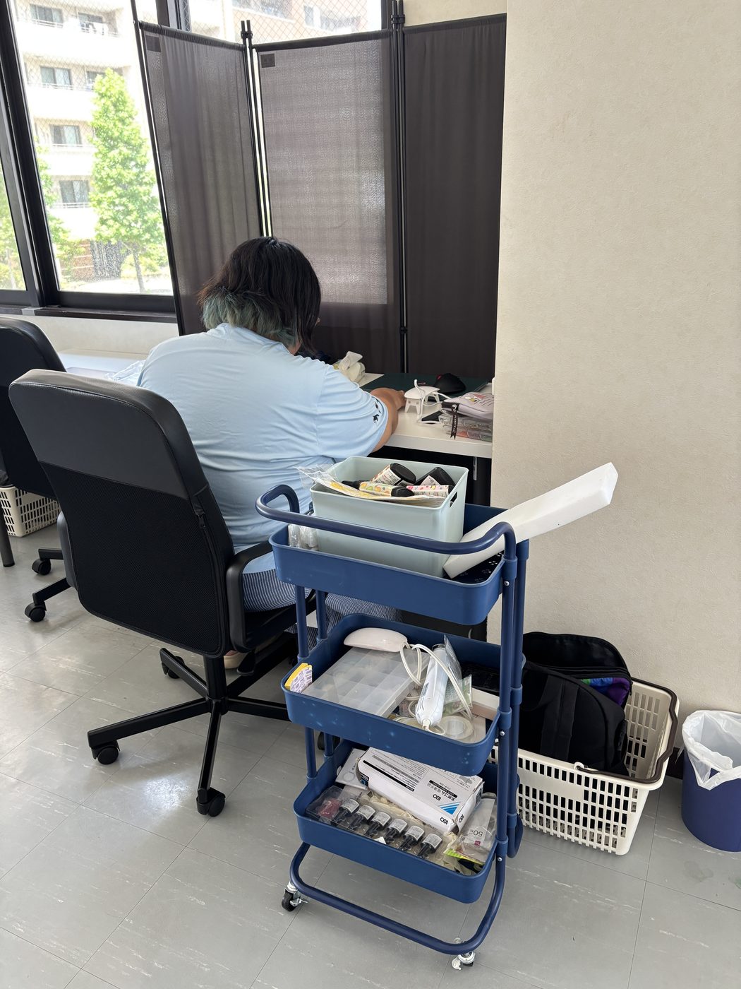 ALOHAの利用者様が窓際の席で、道具をそろえた作業カートのそばで午前の制作に集中して取り組む様子
