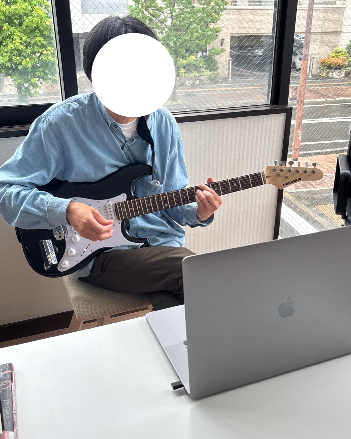窓際の席でエレキギターを構え、ノートパソコンを前に音楽制作に取り組むALOHAの利用者様