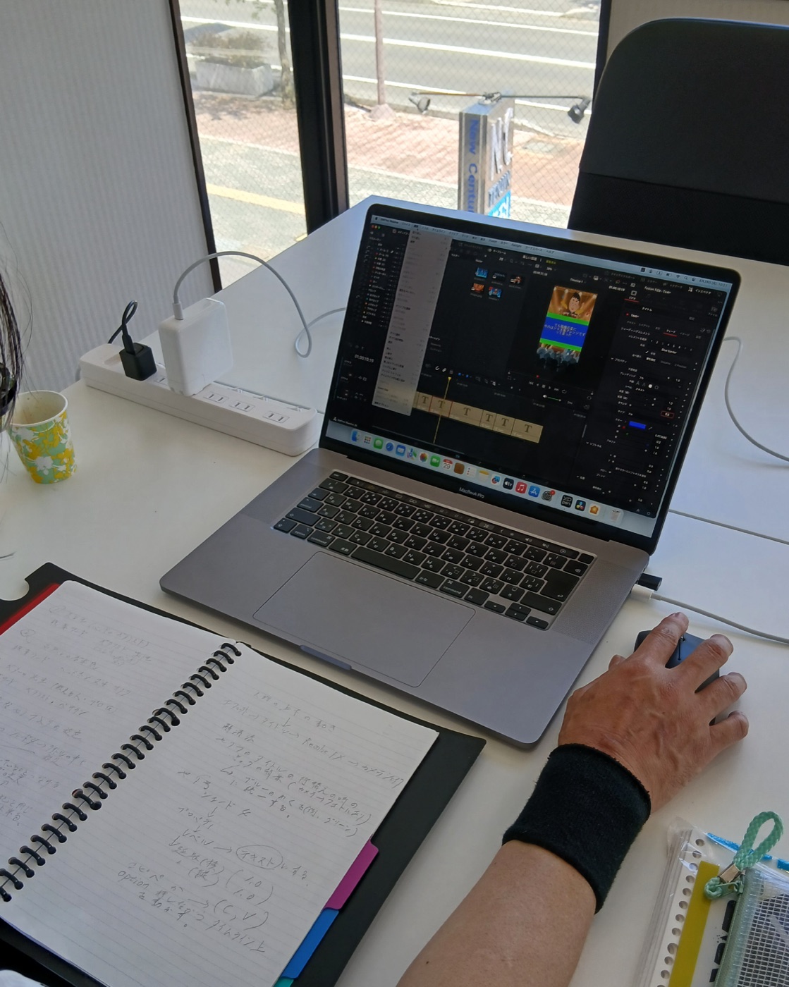 ノートパソコンの編集ソフトでテロップ作業を進める手元と、操作手順を書き留めた手書きのノート